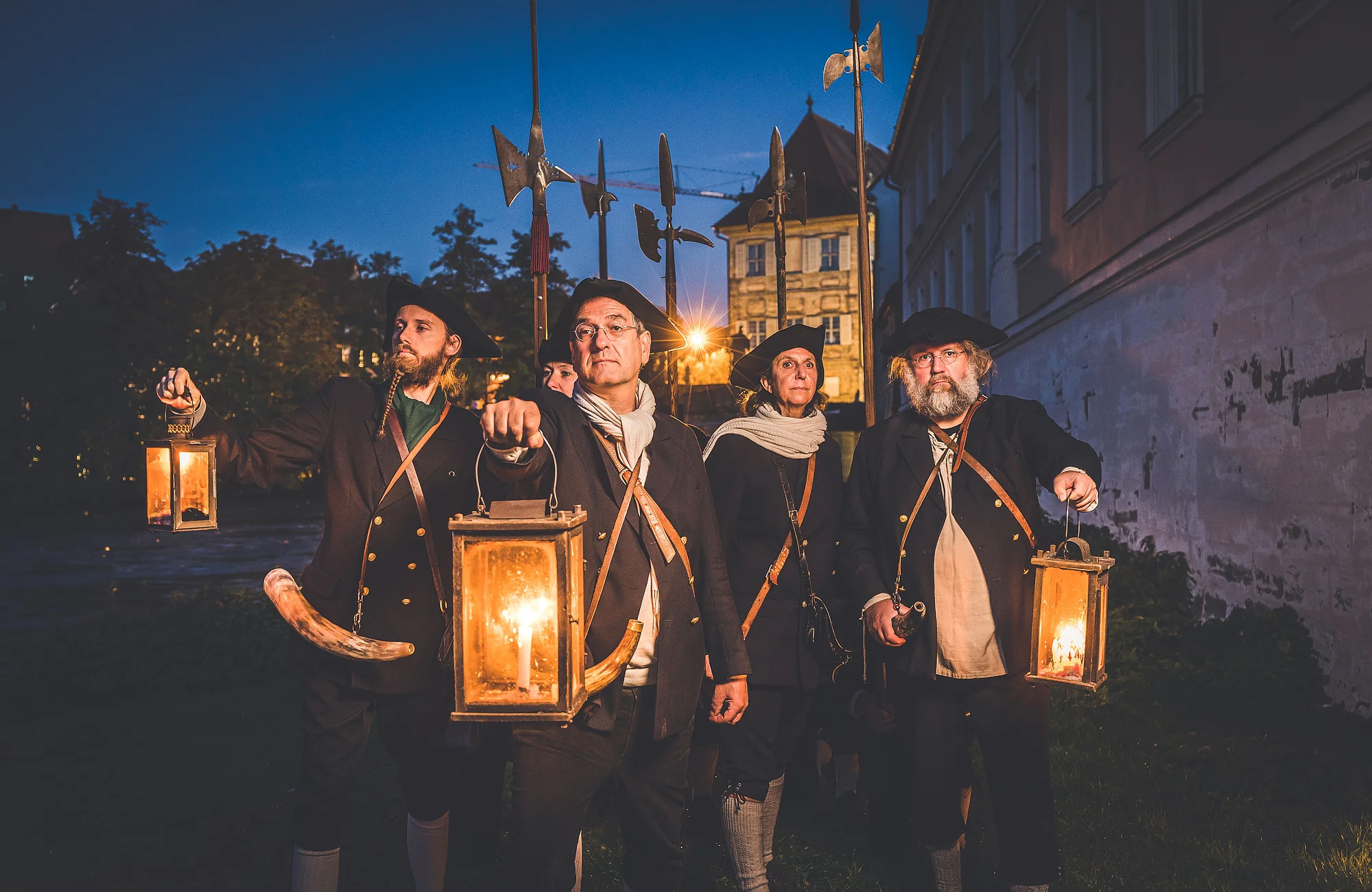 Eine Gruppe von Nachtwächtern steht bei Nacht mit ihren Leuchten und Hellebarden in der Altstadt Bambergs