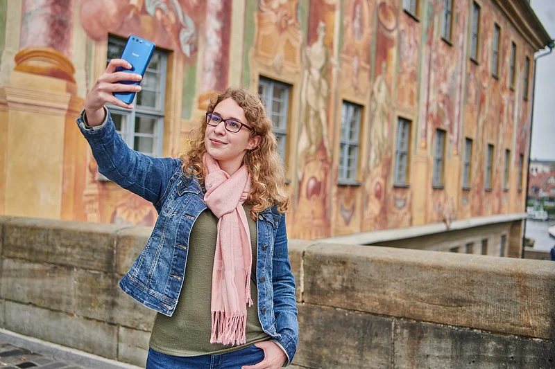 Eine Frau macht ein Selfie auf der Brücke vor dem Alten Rathaus in Bamberg.