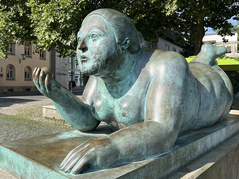 Von den Bambergern liebevoll „Dicke Frau“ oder „Blunnzn“ genannt, ist die Skulptur „Liegende mit Frucht“ des kolumbianischen Künstlers Fernando Botero ein markantes Kunstwerk in Bamberg.